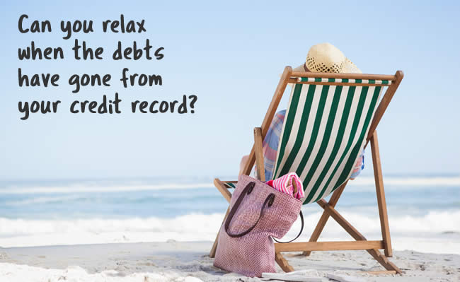 Woman in a deckcair relaxing on a beach - all the debts have gone from her credit record