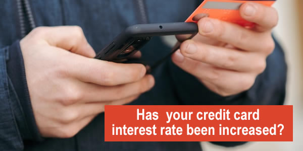 man holding a credit card looking at his phone - what are your options if a UK credit card increases the interest rate?
